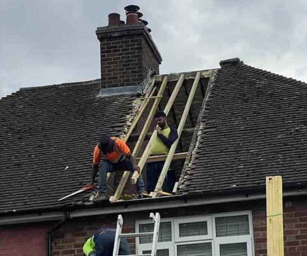 This is a photo of a roof repair being carried out. A section of the roof has been stripped and two roofers are replacing the rafters. Works being carried out by JYT Roofing Hitchin